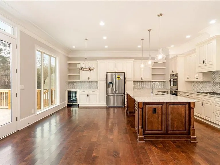 Spacious modern kitchen with white cabinetry, large center island, hardwood flooring, and recessed lighting.