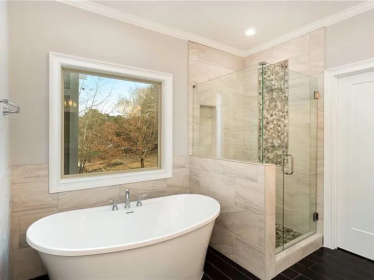 Modern bathroom featuring a freestanding bathtub, large window, and a glass-enclosed walk-in shower with decorative tile accents.