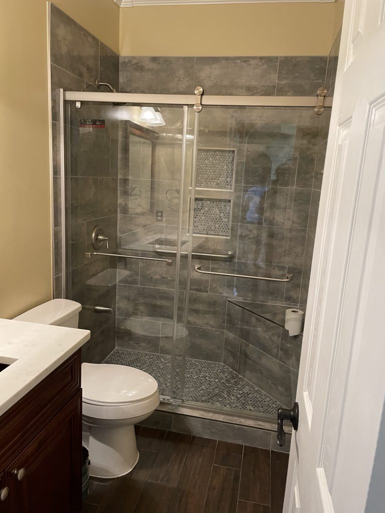 Small modern bathroom with a glass-enclosed shower featuring dark tile and a built-in shower niche, complemented by a wooden vanity and toilet