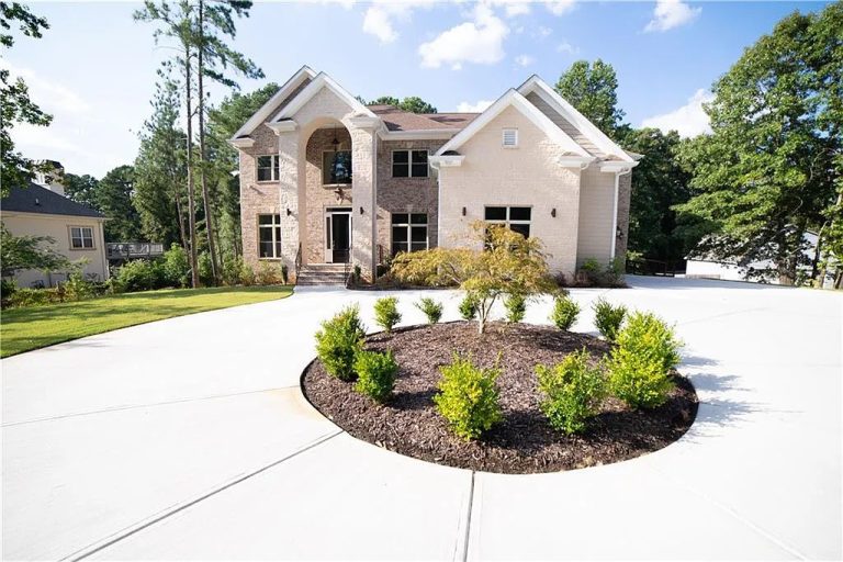 “Large two-story brick home with arched entryway, surrounded by a well-manicured lawn, circular driveway, and central landscaped island with small shrubs and a tree.