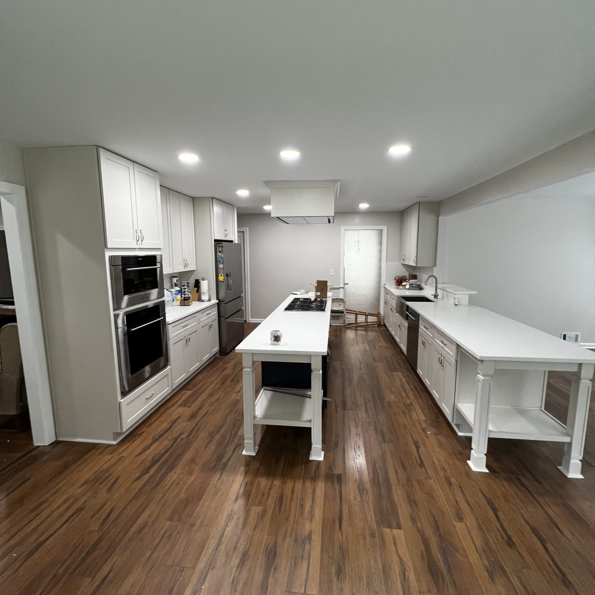 Spacious modern kitchen with white cabinetry, large center island, hardwood flooring, and recessed lighting.